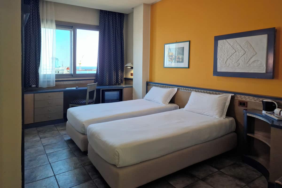 A hotel room with two beds, a desk, a chair, and a window with curtains.