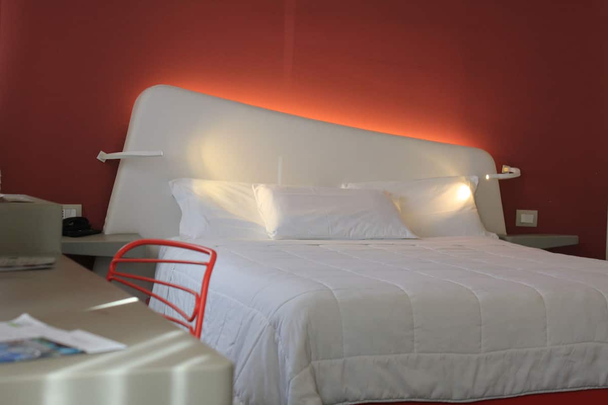 A neatly made bed with white bedding and a red wall behind it.