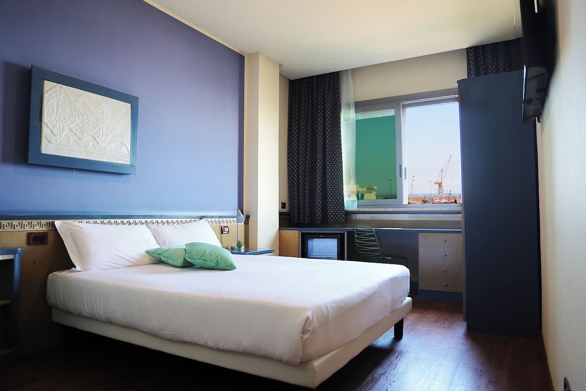A hotel room with a bed, a desk, a window with curtains, and a view of a construction site.