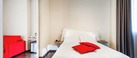 Una habitación de hotel con una cama, un sofá rojo, una mesita de noche y una ventana con cortinas.