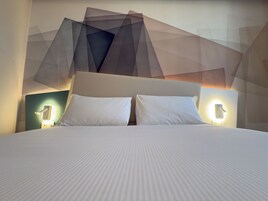Un letto con una testiera bianca e due lampade ai lati.