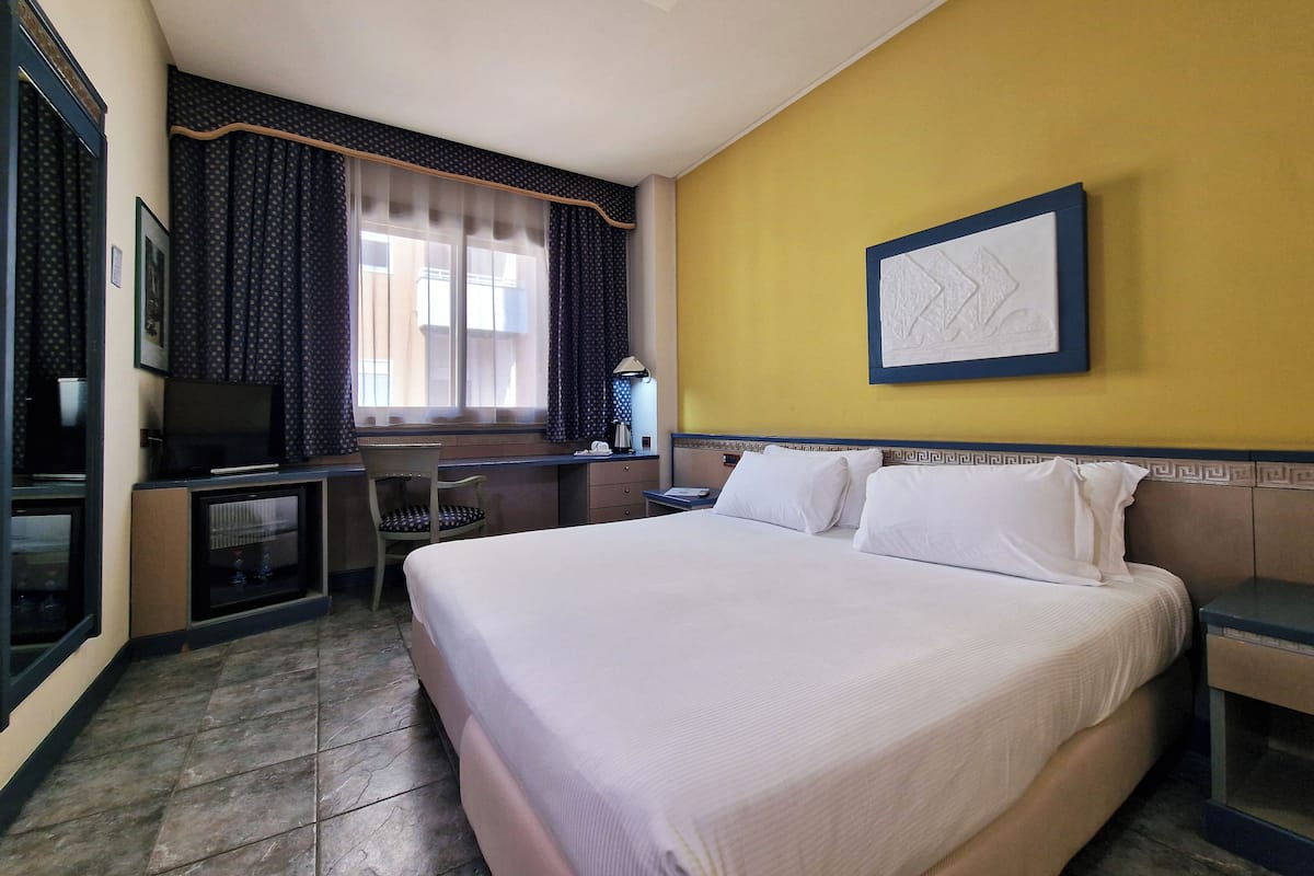 A hotel room with a large bed, a desk with a chair, a television, and a window with curtains.