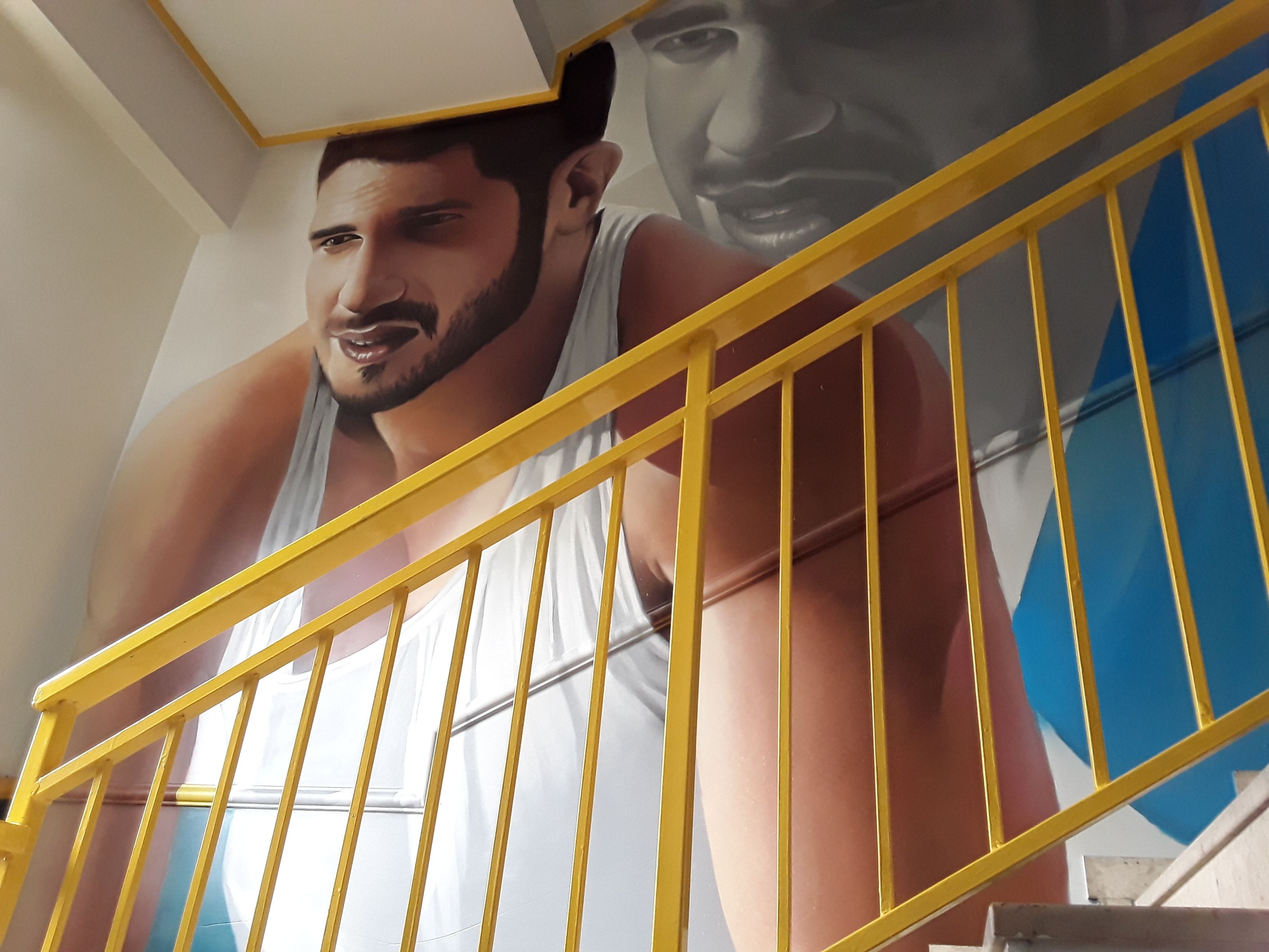 Una escalera con barandas amarillas y un cartel grande de una persona con camiseta blanca.
