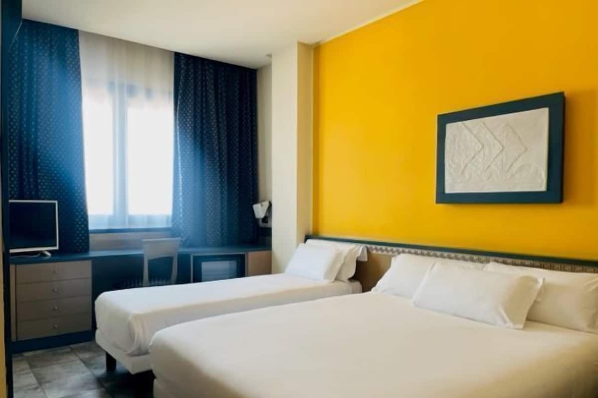 A hotel room with two beds, a desk with a computer, and a window with curtains.