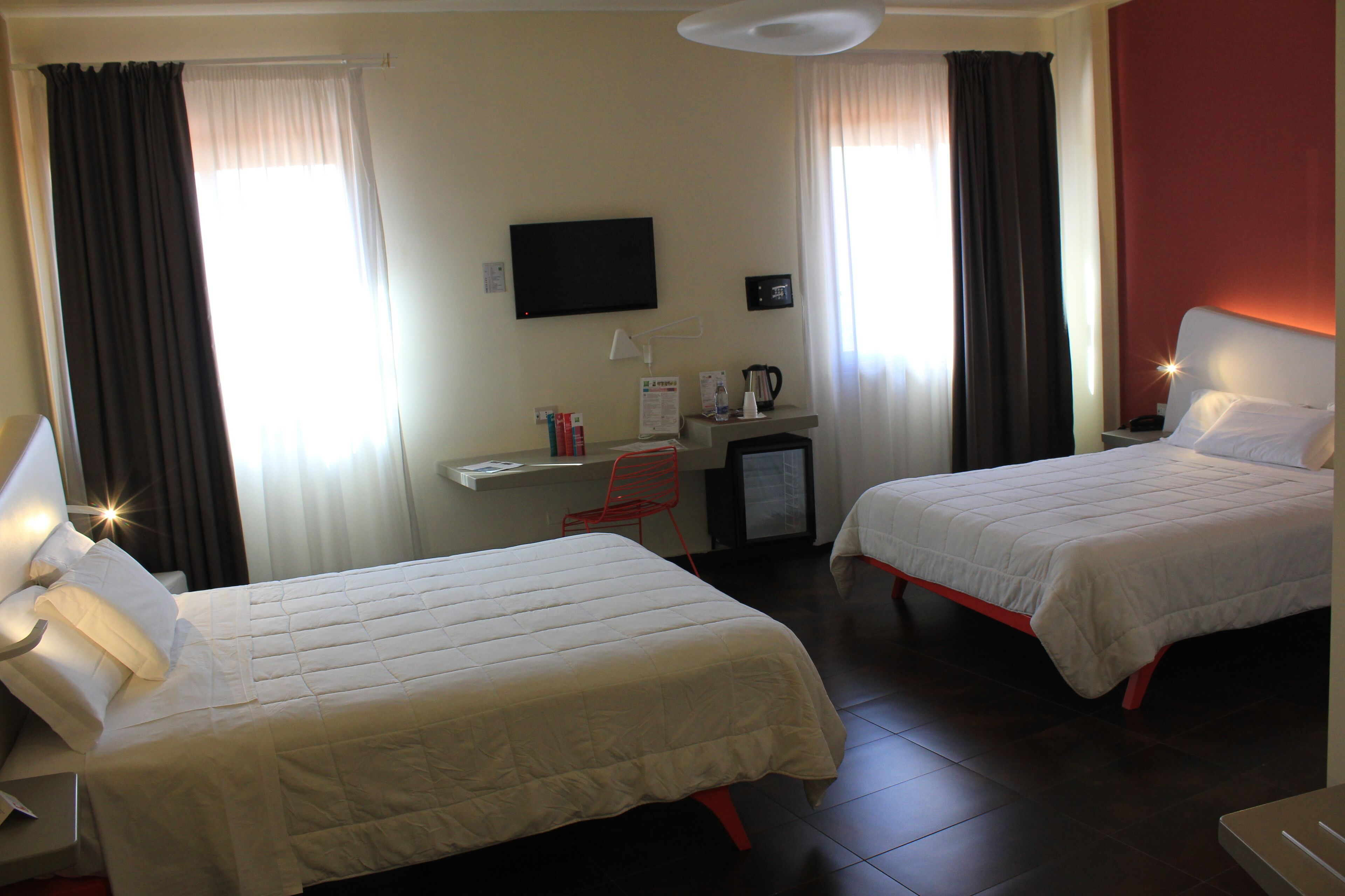 Habitación de hotel con dos camas, un escritorio, una silla, un televisor y una mesita con un hervidor.