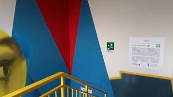 A staircase with yellow railings and a blue and red wall. There is an emergency exit sign and a notice on the wall.