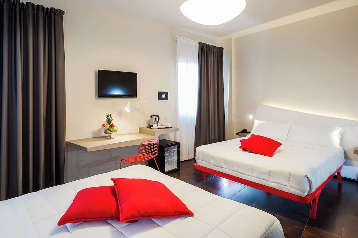 A hotel room with two beds, a desk, a chair, a TV, and a small kitchenette.