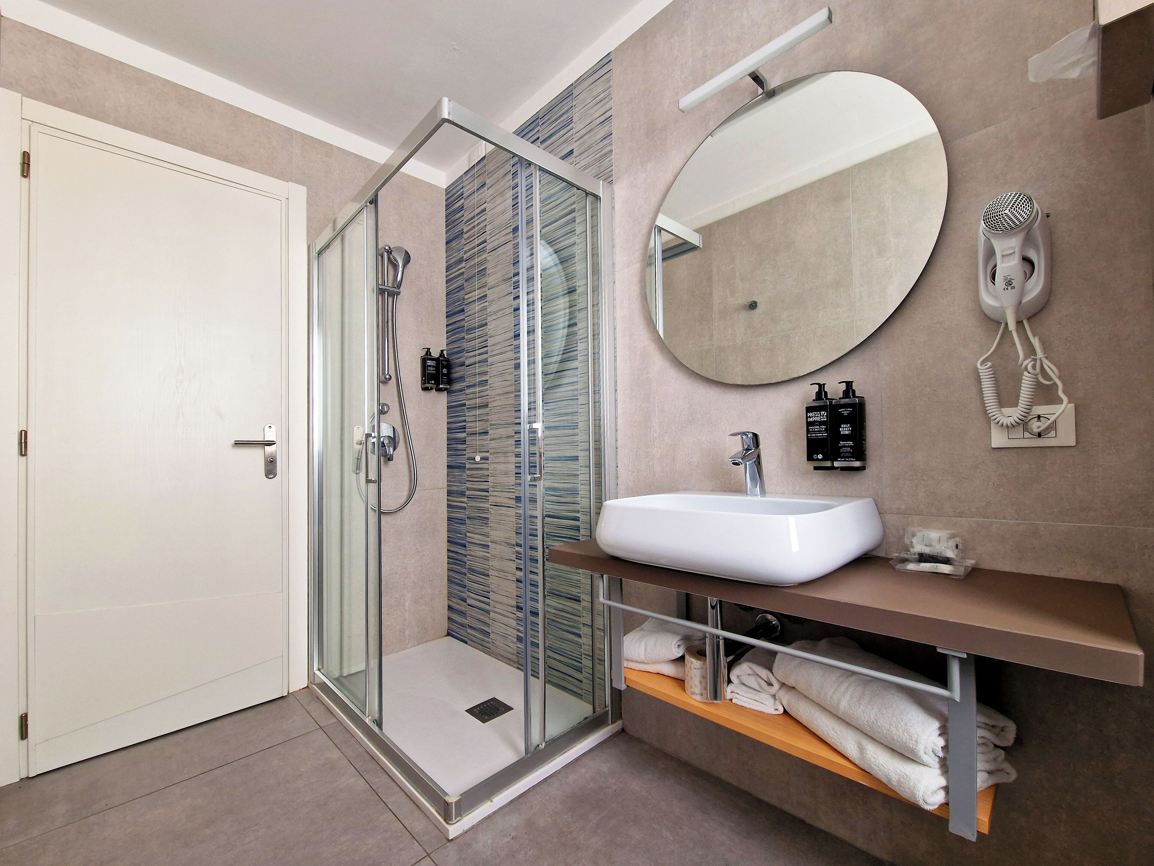 A modern bathroom with a glass-enclosed shower, a white sink, and a mirror above it.