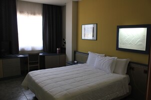 Una camera d'albergo con un letto, una scrivania, una sedia, una televisione e un quadro appeso al muro.
