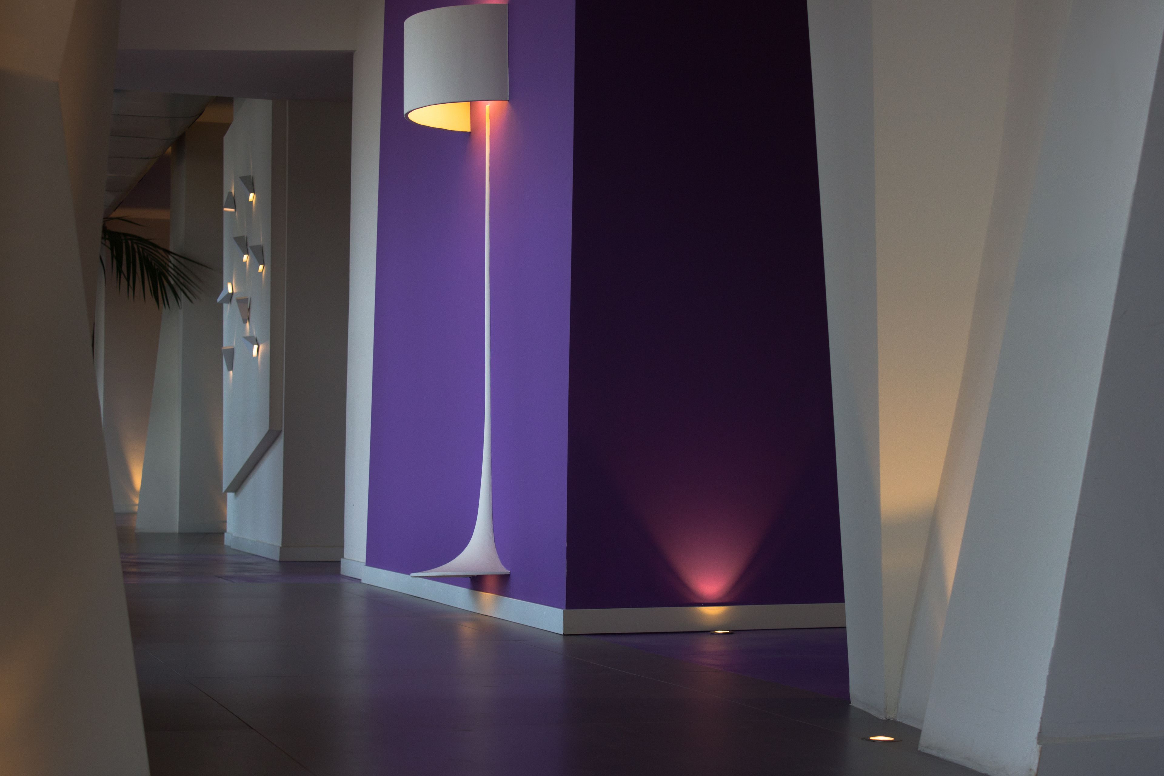 A modern hallway with a purple accent wall, a tall floor lamp, and a staircase in the background.