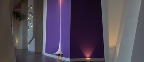 A modern hallway with a purple accent wall, a tall floor lamp, and a staircase in the background.