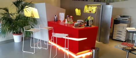 A modern reception area with a red counter, white chairs, a potted plant, and a printer.