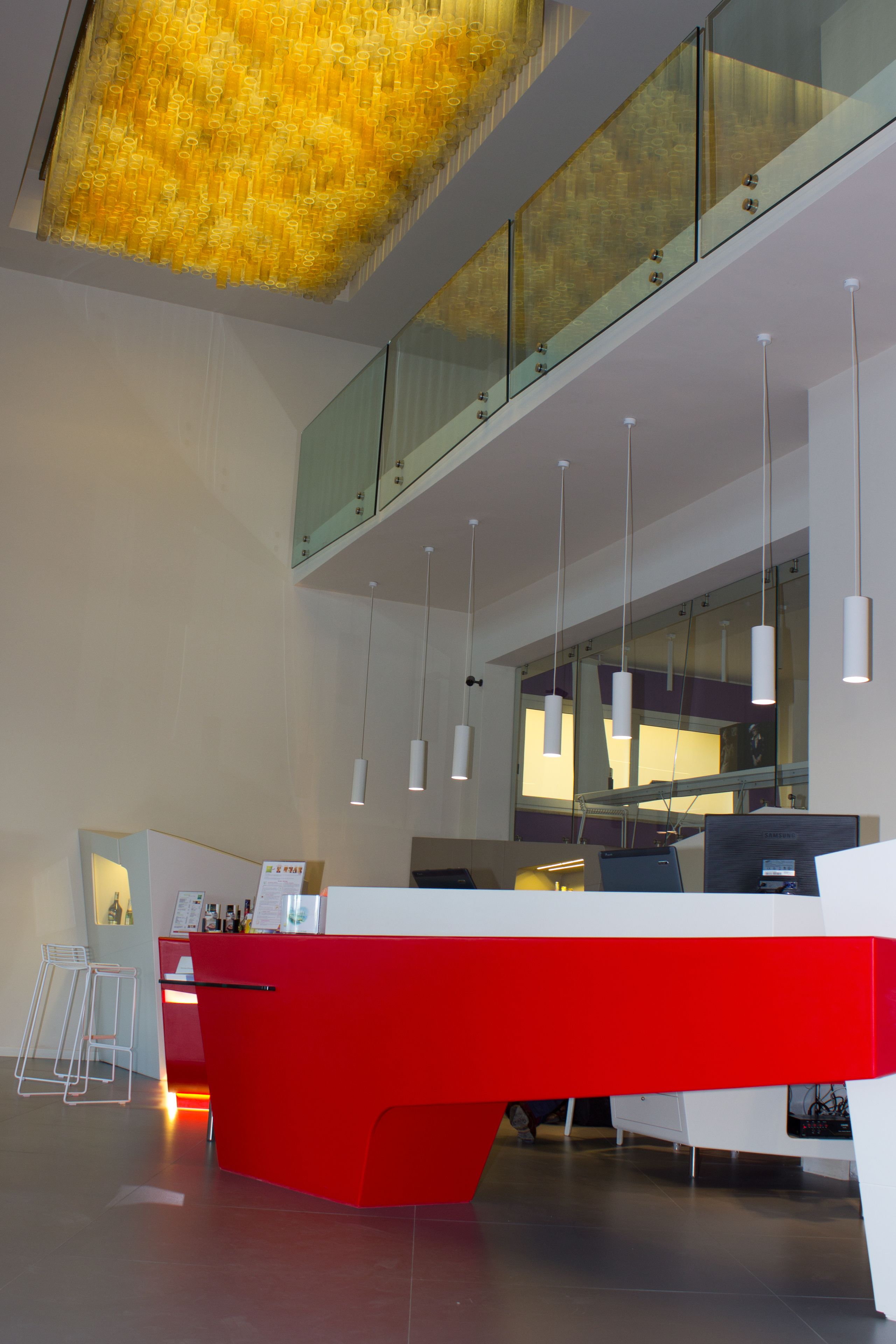 A modern reception desk with a red and white color scheme, glass railings, and pendant lighting.