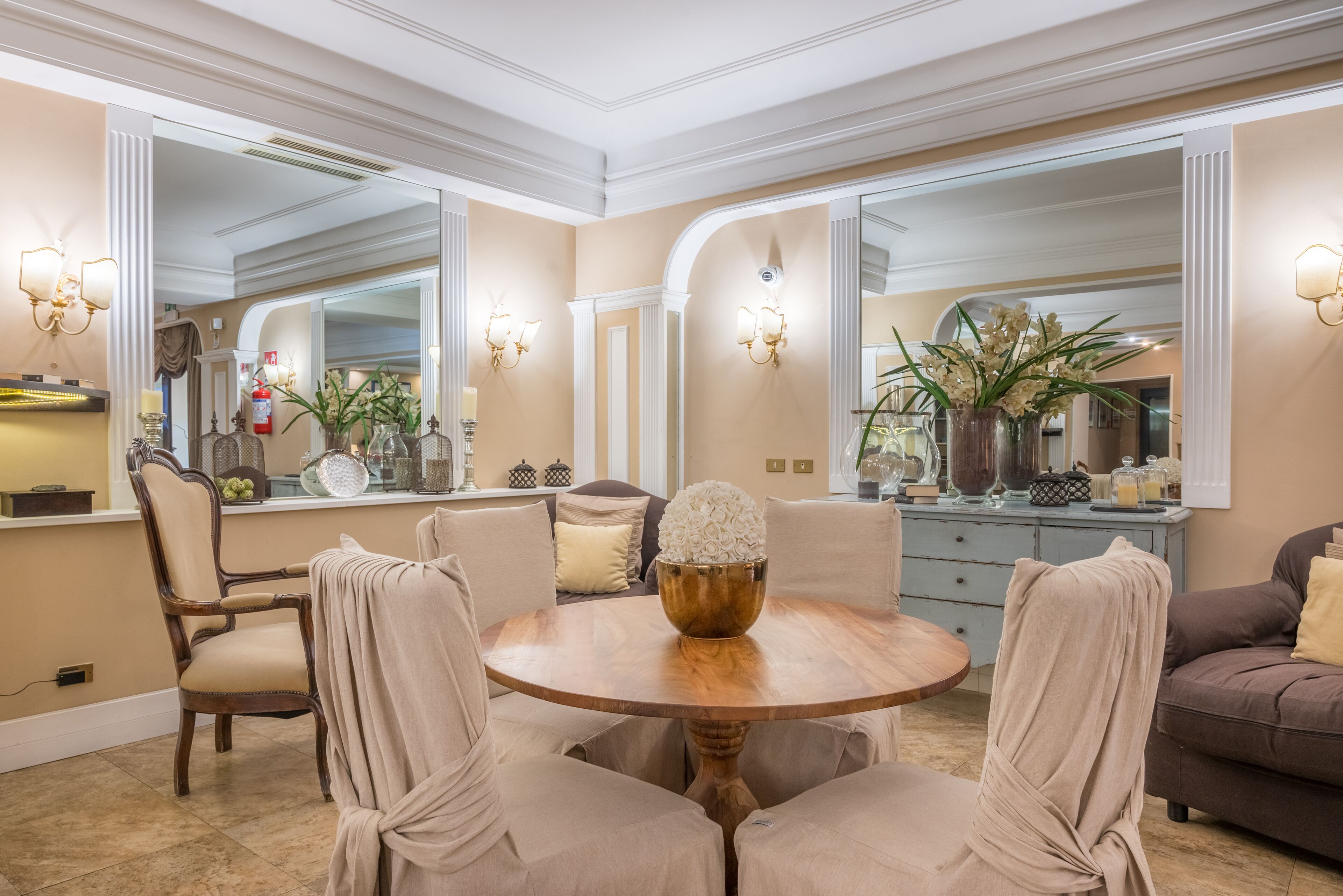 A dining area with a round wooden table, beige upholstered chairs, and a decorative centerpiece.