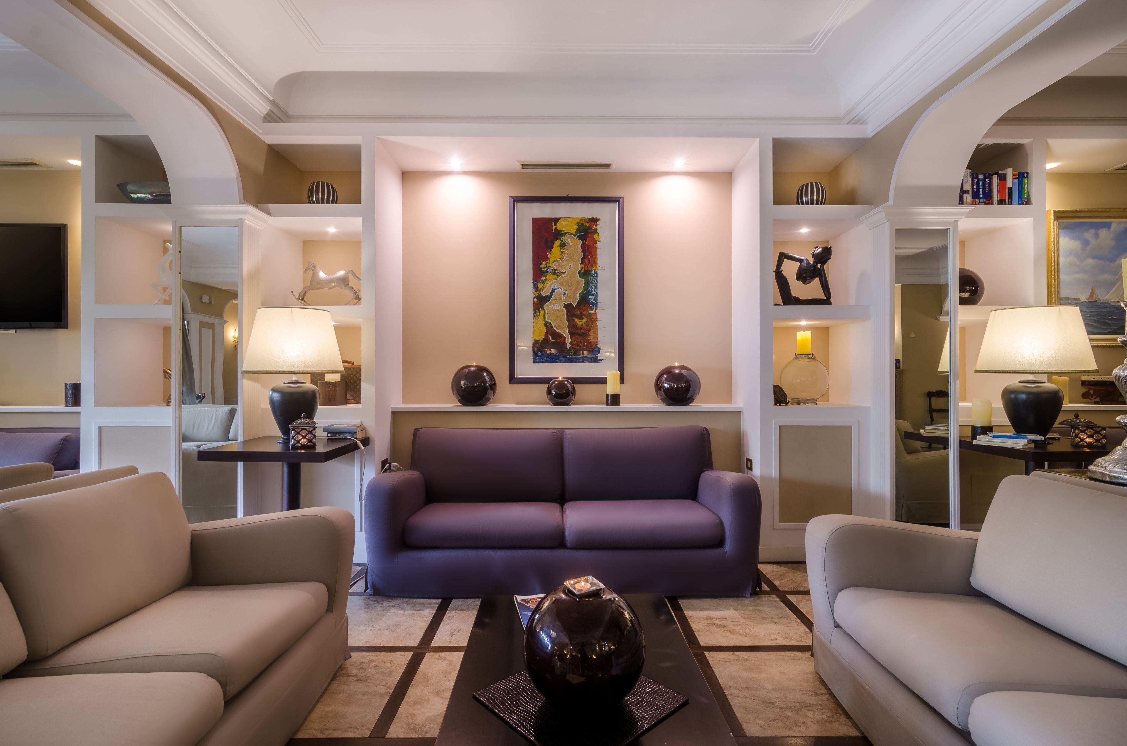 A modern living room with a purple sofa, beige armchairs, a coffee table, and decorative items on shelves.