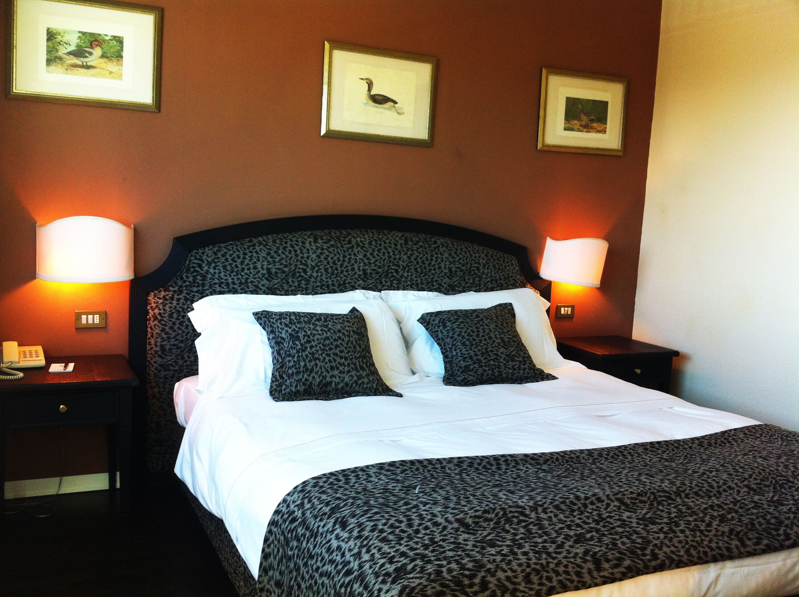 A hotel room with a bed, two nightstands, and three framed pictures on the wall.