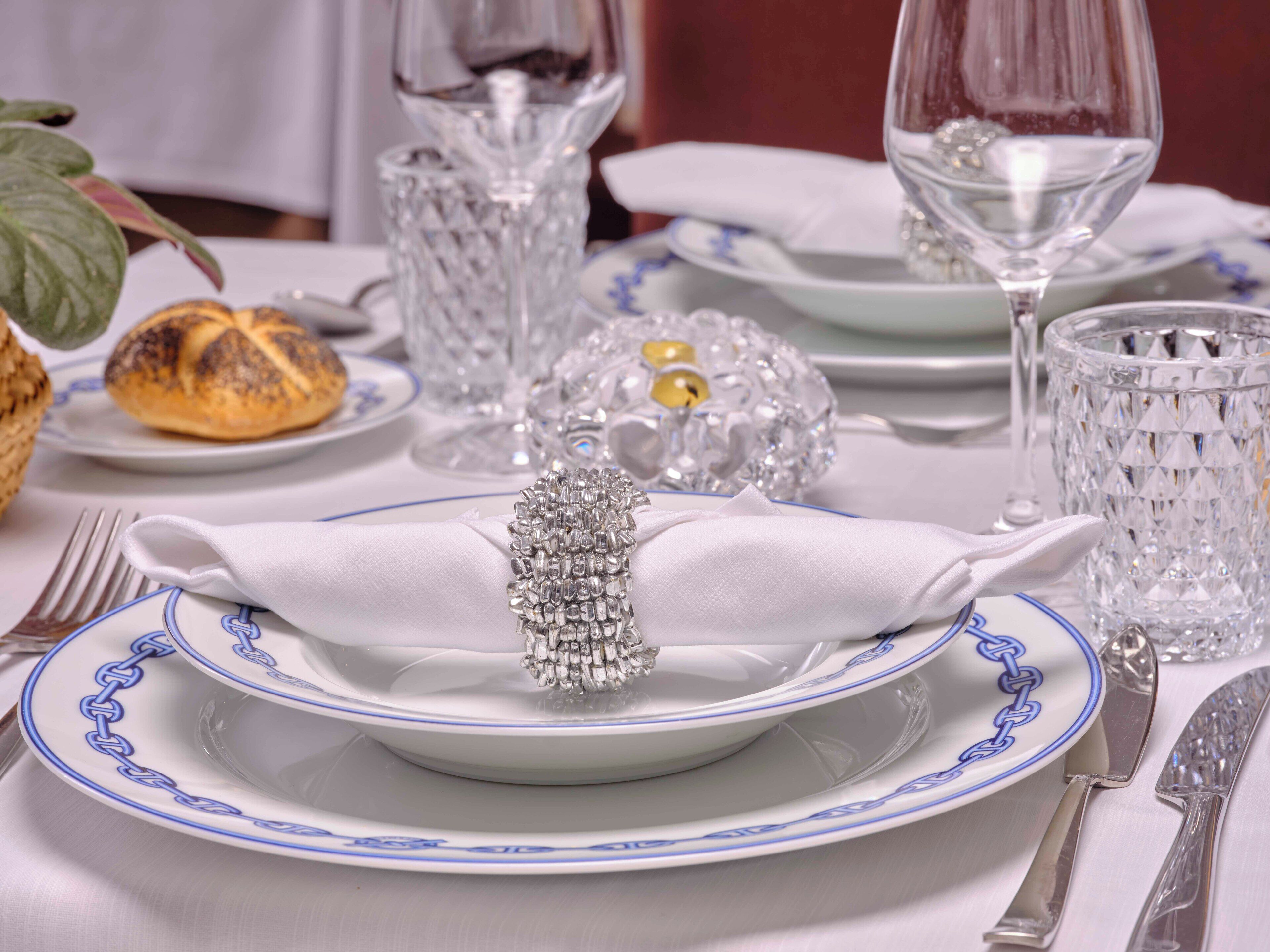 Mesa formal dispuesta para comer, con platos blancos, vajilla de borde azul, cristalería y cubiertos.