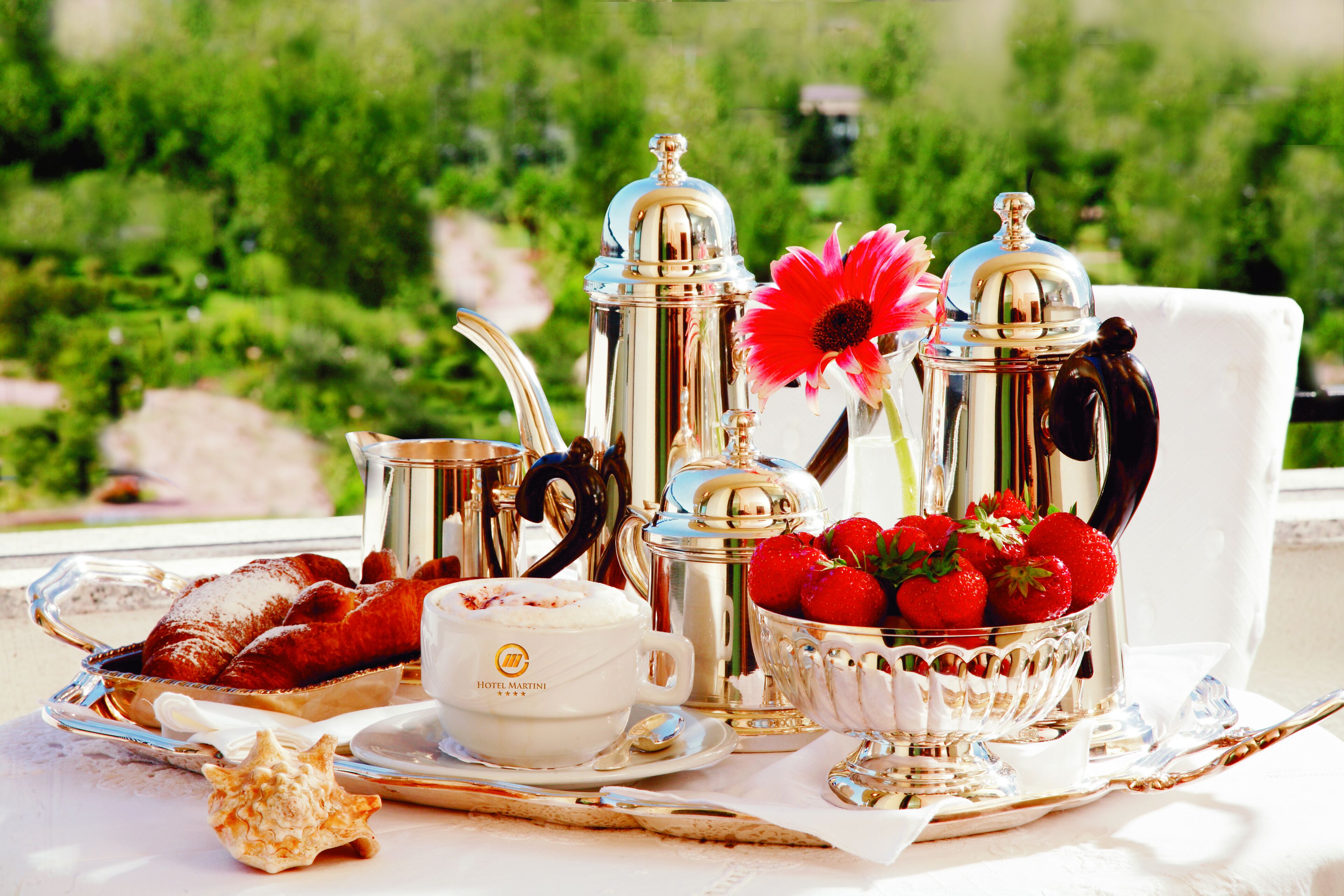 Un plateau de petit-déjeuner avec des viennoiseries, du café et des fraises, posé sur une table offrant une vue panoramique.