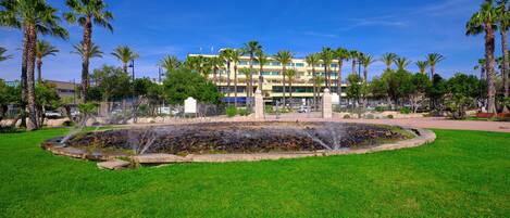 A landscaped area with a fountain, palm trees, and a building in the background.