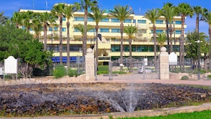 A hotel with multiple floors, palm trees, and a fountain in the foreground.