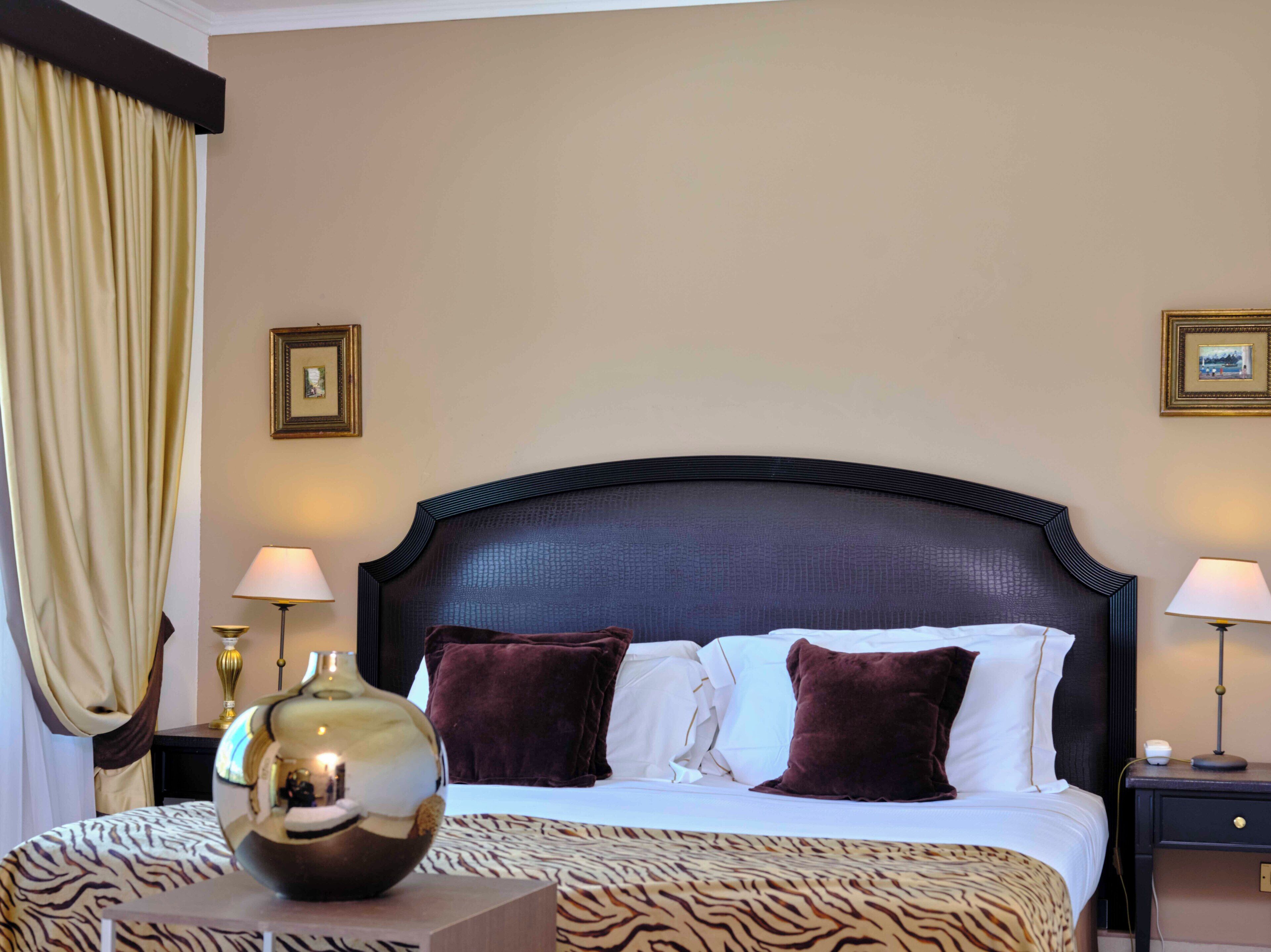 A hotel room with a large bed, two bedside lamps, a decorative vase, and a zebra-patterned throw.