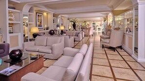 A spacious living area with a large sofa set, a coffee table, and a glass-top table with a magazine. There are decorative items on shelves and a dining area in the background.