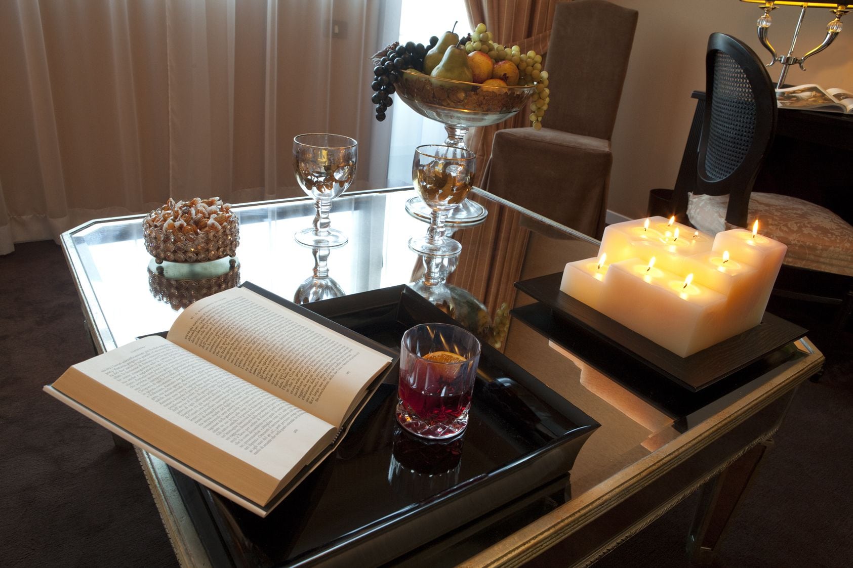 Une table en verre avec un livre, une bougie et un panier de fruits.