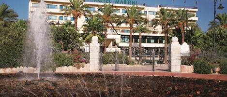 A hotel with a fountain, palm trees, and a clear sky.