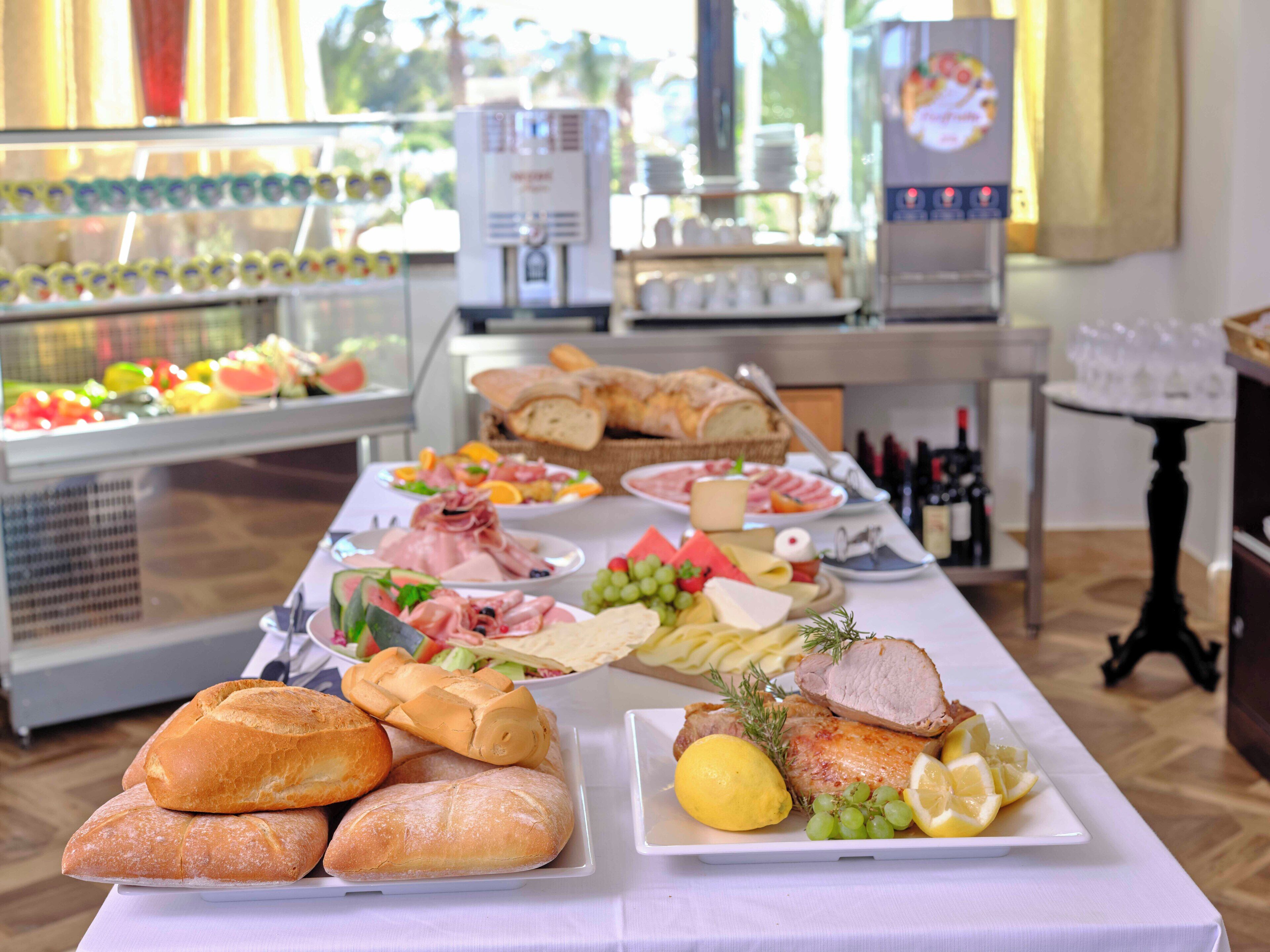 A buffet table with various food items including bread, meats, cheeses, and fruits.