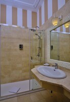Un baño moderno con ducha de vidrio, un espejo grande y piso de baldosas color beige.