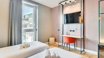 Une chambre d’hôtel avec deux lits, un bureau, une chaise, une télévision et une fenêtre avec des rideaux.