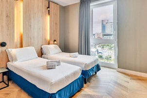 Camera d'albergo con due letti, rivestimenti in legno sulle pareti, un'ampia finestra con vista sulla città e un design moderno.