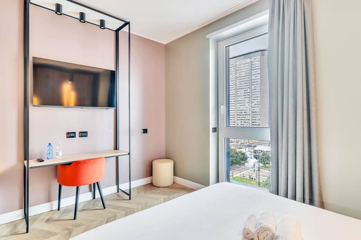 Ein Hotelzimmer mit einem Bett, einem Schreibtisch mit Stuhl, einem Fernseher und einem Fenster mit Vorhängen.