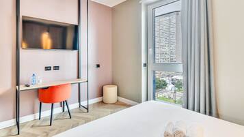 A hotel room with a bed, a desk with a chair, a TV, and a window with curtains.