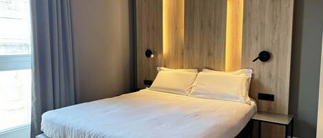 Un dormitorio moderno con cama, panel de madera y luces empotradas.