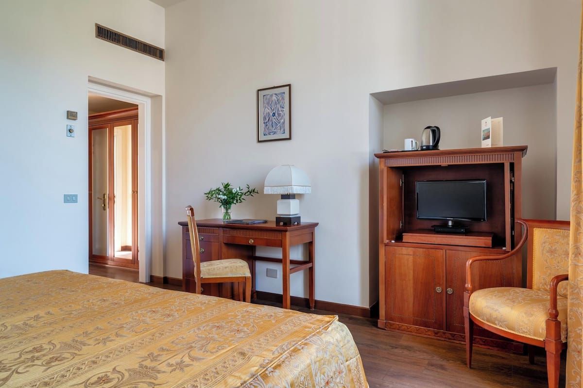 Una habitación de hotel con una cama, un escritorio con lámpara, televisión y una silla.