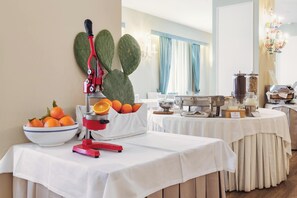A buffet setup with a fruit press, a bowl of oranges, and a coffee machine. - Excelsior Palace Hotel (Taormina)