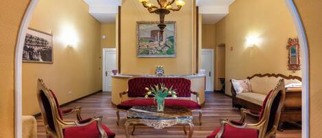A grand lobby with a chandelier, red upholstered sofas, and a marble coffee table.