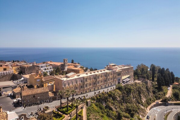 A coastal town with historic architecture, a prominent building with a clock tower, and a view of the sea. - Excelsior Palace Hotel (Taormina)