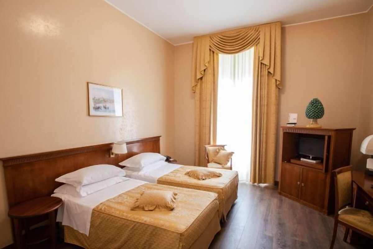 A hotel room with two beds, a TV cabinet, and a window with curtains.