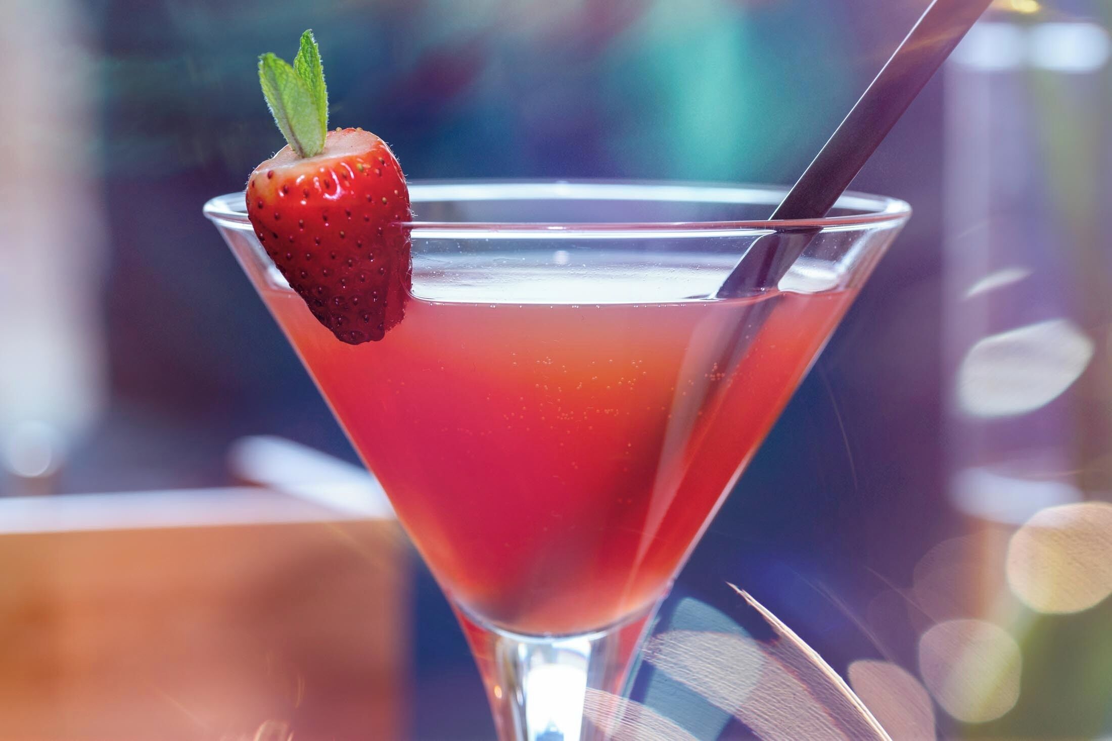 Een martini glas met een aardbeien decoratie en een rietje.
