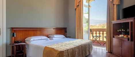 A hotel room with a large bed, a wooden headboard, a nightstand, a TV, a cabinet with flowers, and a balcony with a view.