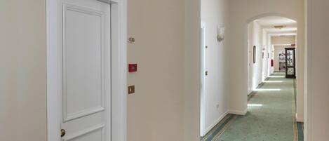 A hallway with a white door, a fire alarm, and a carpeted floor.