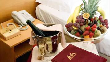 Ein Hotelzimmer mit einem Bett, einem Nachttisch mit Telefon, einer Champagnerflasche, einem Weinglas und einer Obstschale.