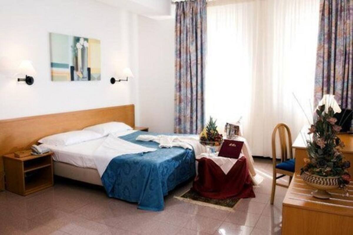Ein Hotelzimmer mit einem Bett, einem Nachttisch, einem Schreibtisch mit Stuhl und einem Fenster mit Vorhängen.