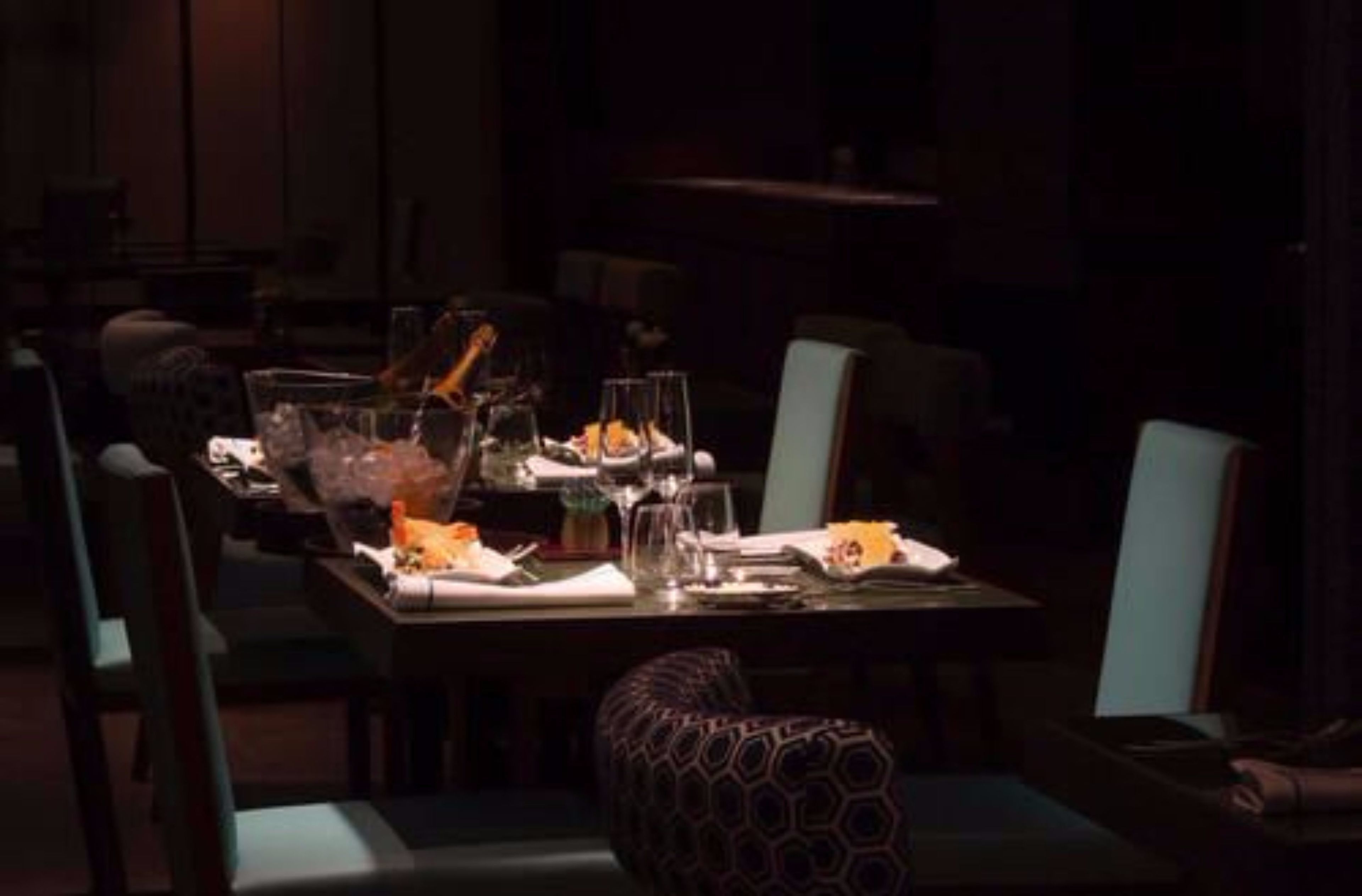 Un restaurante tenuemente iluminado con una larga mesa dispuesta para cenar, rodeada de sillas.