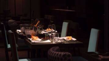 Un restaurante tenuemente iluminado con una larga mesa dispuesta para cenar, rodeada de sillas.