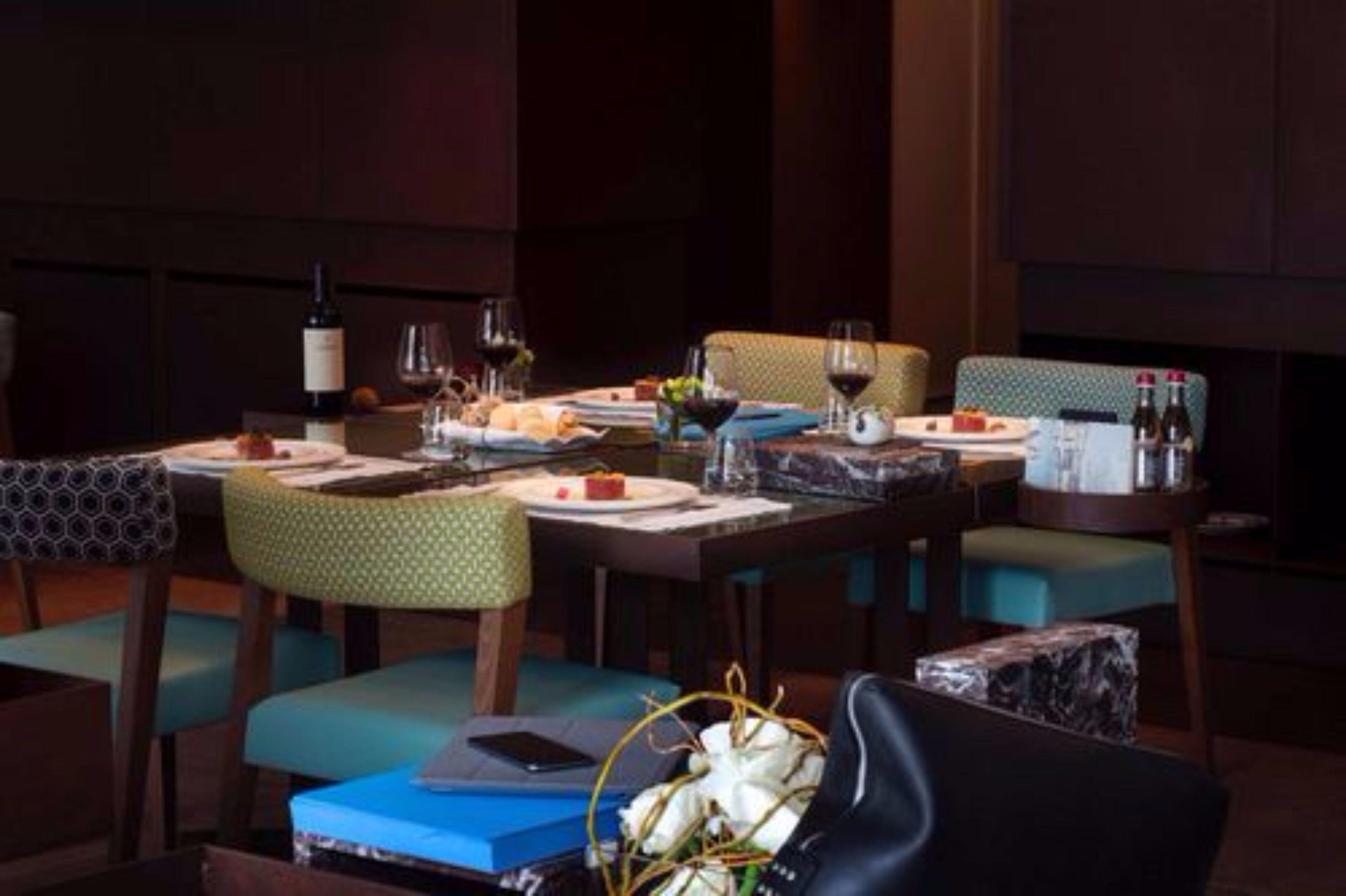 A dining area with a table set for two, featuring a bottle of wine, glasses, and a basket of flowers.