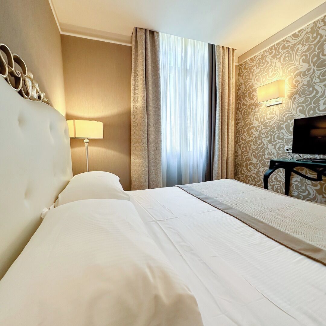 Habitación de hotel con una cama grande, un escritorio con televisor, una lámpara y una ventana con cortinas.