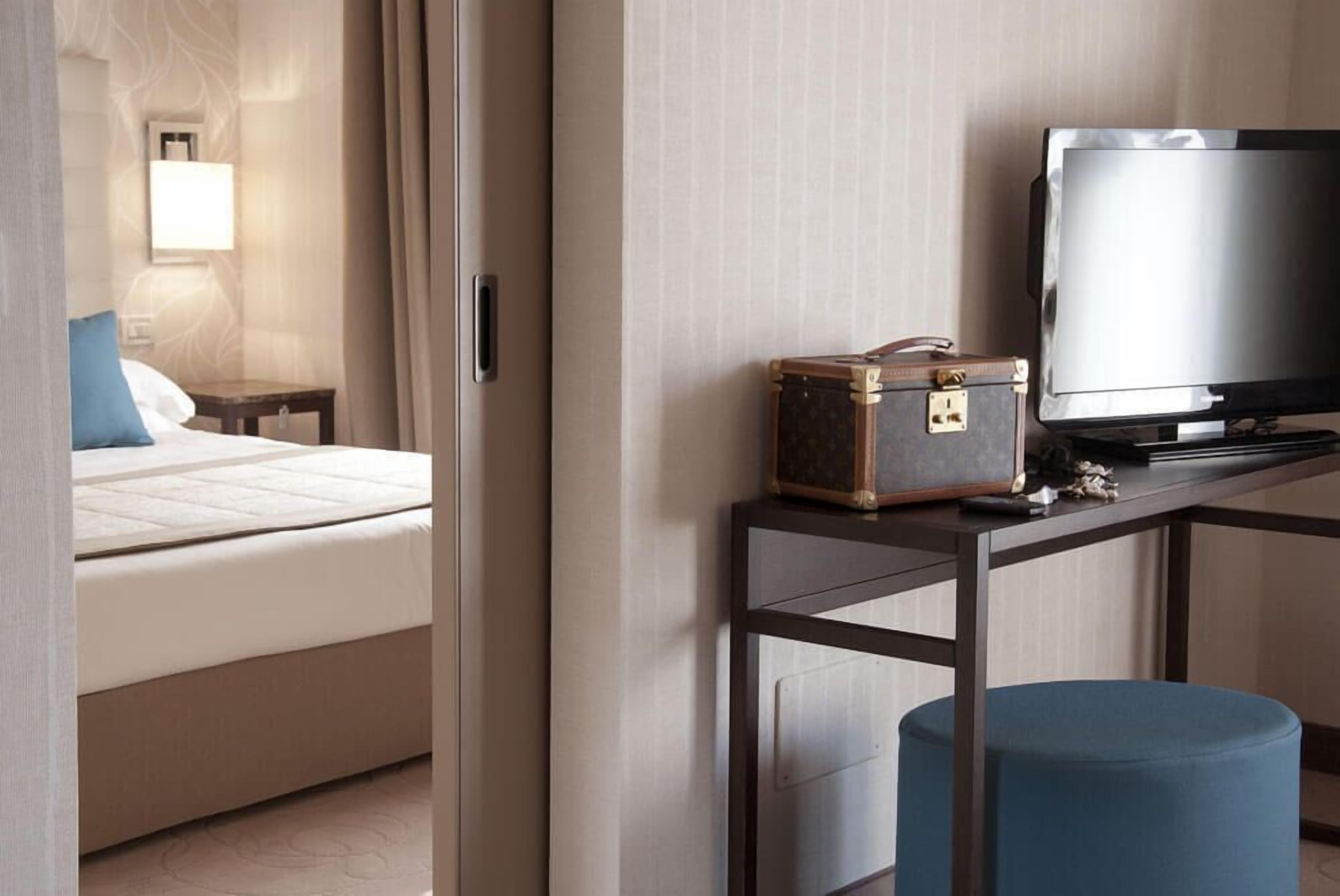 Una camera d'albergo con un letto, una televisione, una valigia e un tavolino.